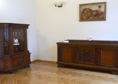 Salonik Hrabiego, po lewej zabytkowa serwantka wykonana z drewna, po prawej zabytkowa komoda z drewna. Nad komodą wisi obraz martwej natury.