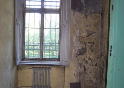 Okno z otwartą, zniszczona wewnetrzna okiennicą. Ściany i podłoga obdrapane i zniszczone.