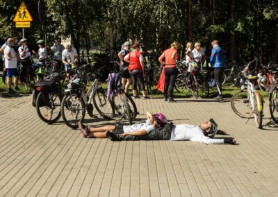 Kilku rowerzystów leżących na chodniku odpoczywa podczas postoju.