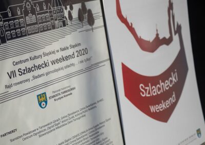 Plakat inforujący o partnerach, sponsorach oraz patronach rajdu, stojący obok plakatu z logo Szlacheckiego Weekendu.