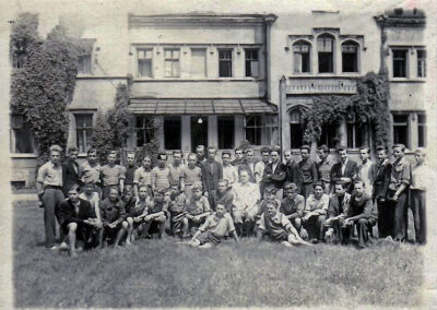 Grupa chłopców i mężczyzn na trawniku przed pałacem w latach pięćdziesiątych.