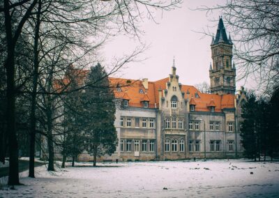 Pałac w nakle Śląskim zimą. Z lewej i prawej strony lekko przysłaniają go drzewa.