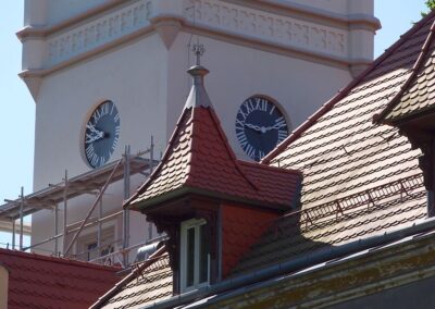 Dwa zegary i fragment rusztowań na wieży pałacu. Z przodu fragment dachu.