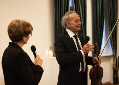 Z lewej strony obrócona bokiem kobieta z mikrofonem. Po prawej stronie z altówką w lewej ręce uśmiechnięty Ulrich von Wrochem mówi coś do mikrofonu.
