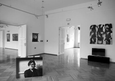 Czarno-białe zdjęcie sali wystawowej. Obrazy na Ścianach. Jeden obraz oparty na podłodze.