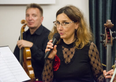 Wiolonczelistka Katarzyna Biedrowska mówiąca coś do mikrofonu. Za nią z altówką w ręce muzyk Jarosław Marzec.