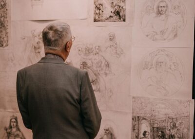 A man standing with his back is looking at cards with drawings pinned to the exhibition wall.