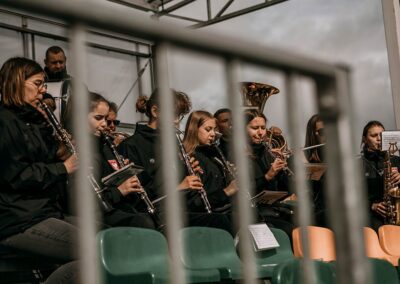 Orkiestra dęta siedzi na trybunach i gra koncert.