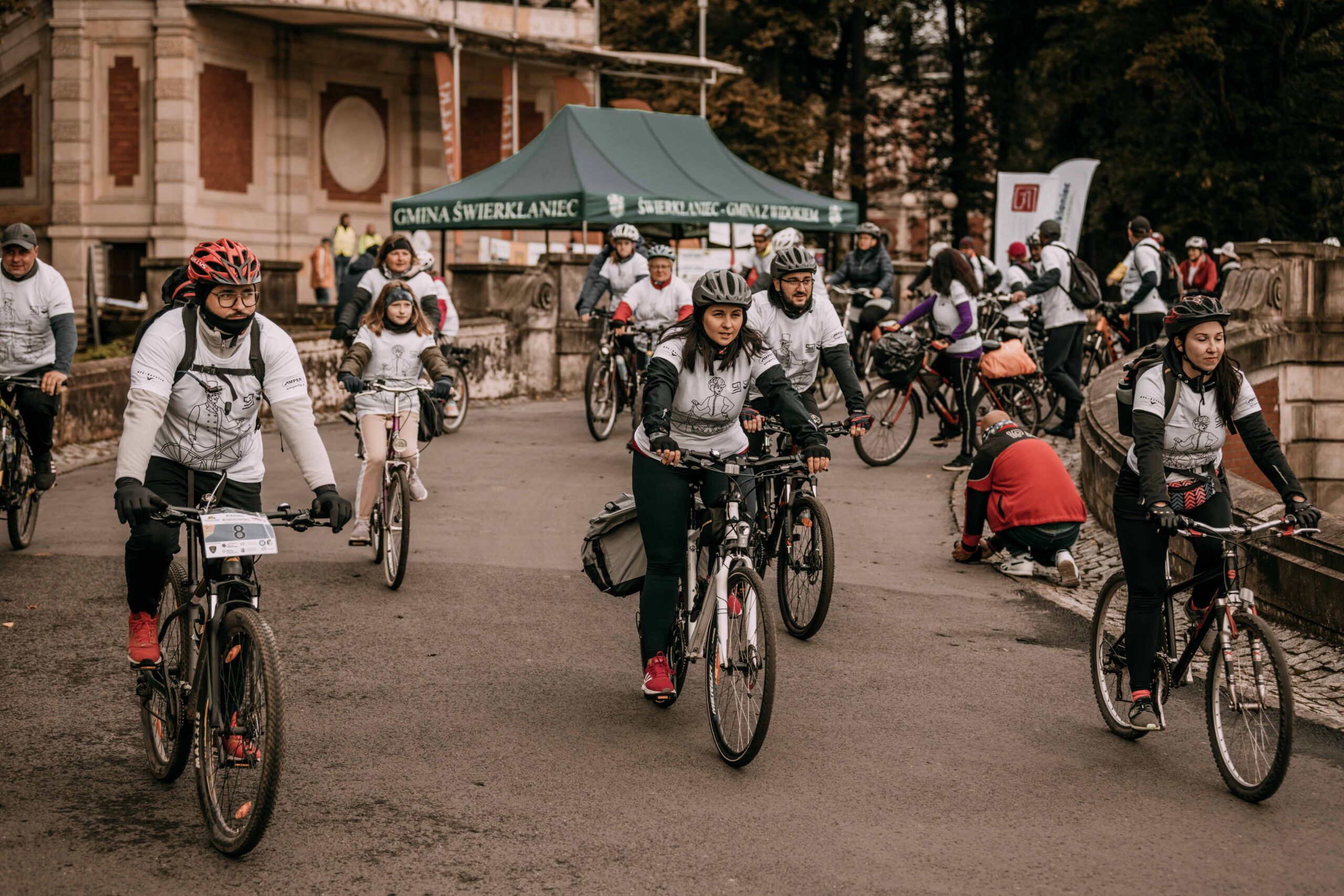 Grupa osób w koszulkach IX Rajdu rowerowego wyrusza na swoich rowerach spod Pałacu Kawalera w Świerklańcu na IX Rajd Rowerowy podczas szlacheckiego weekendu.