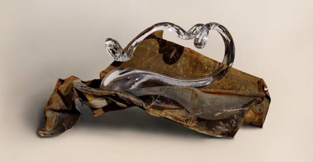 Rzeźba będąca połączeniem zardzewiałego metalu pogiętego jak kartka papieru oraz giętej szklanej rurki.