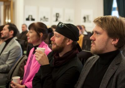 Ludzie na widowni popijający napoje z papierowych kubków i słuchający wykładu podczas konferencji wystawy "Terytoria Materii".