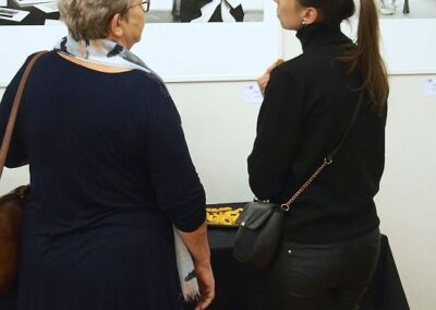 Dwie kobiety stoją tyłem i oglądają portrety artystów kultury śląskiej na wernisażu wystawy "Siła detalu".