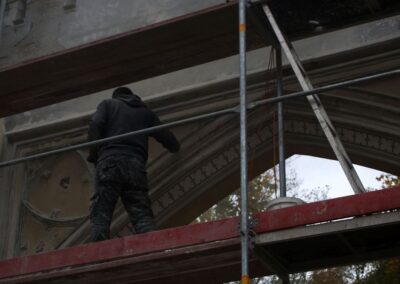 Mężczyzna stojący na rusztowaniu pracuje przy renowacji bramy wjazdowej.