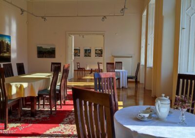 Sala wystawowa, na podłodze kolorowy dywan. Na środku sali i po bokach rozstawione stoły nakryte obrusami.
