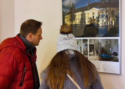 Kobieta i mężczyzna w zimowych kurtkach oglądaja zdjęcia z wystawy Splendro odzyskany.