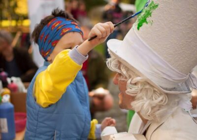 Dziecko malujące biały cylined na głowie mężczyzny.