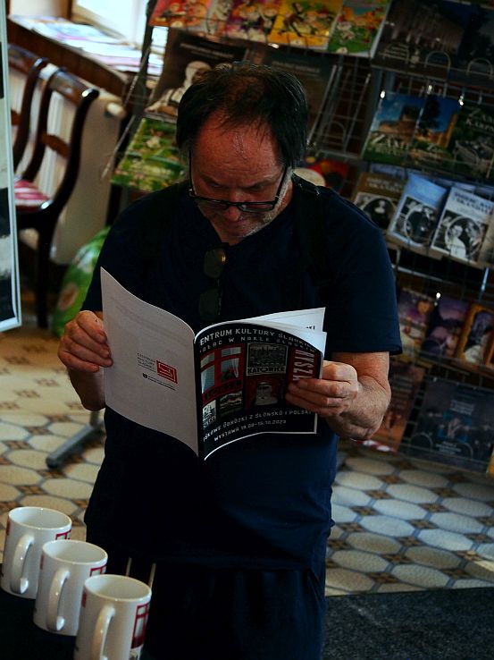 Leszek Jamrozik w czarnej koszuli przegląda katalog z wystawy.