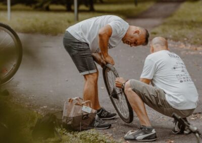 Dwóch mężczyzn naprawiających odkręcone koło roweru.