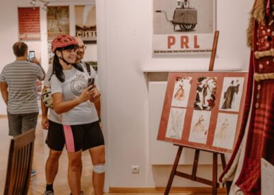 Ludzie w kaskach rowerowych oglądają plakaty Ryszarda Kai wiszące w salach wystawowych.