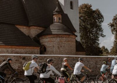 Grupa rowerzystów jadąca wzdłuż muru, za którym widać kościół św. Marcina.