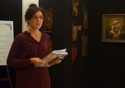 Anna Kempa-Gąsior trzymająca w rękach kilka kartek stoi na tle wystawy ikon.