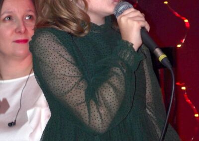 Dziewczynka w ciemnozielonej sukience z mikrofonem w ręce.