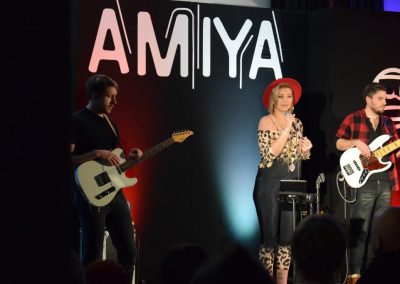 Amiya podczas koncertu, z lewej strony gitarzysta, z prawej basista. W tle napis Amyia.